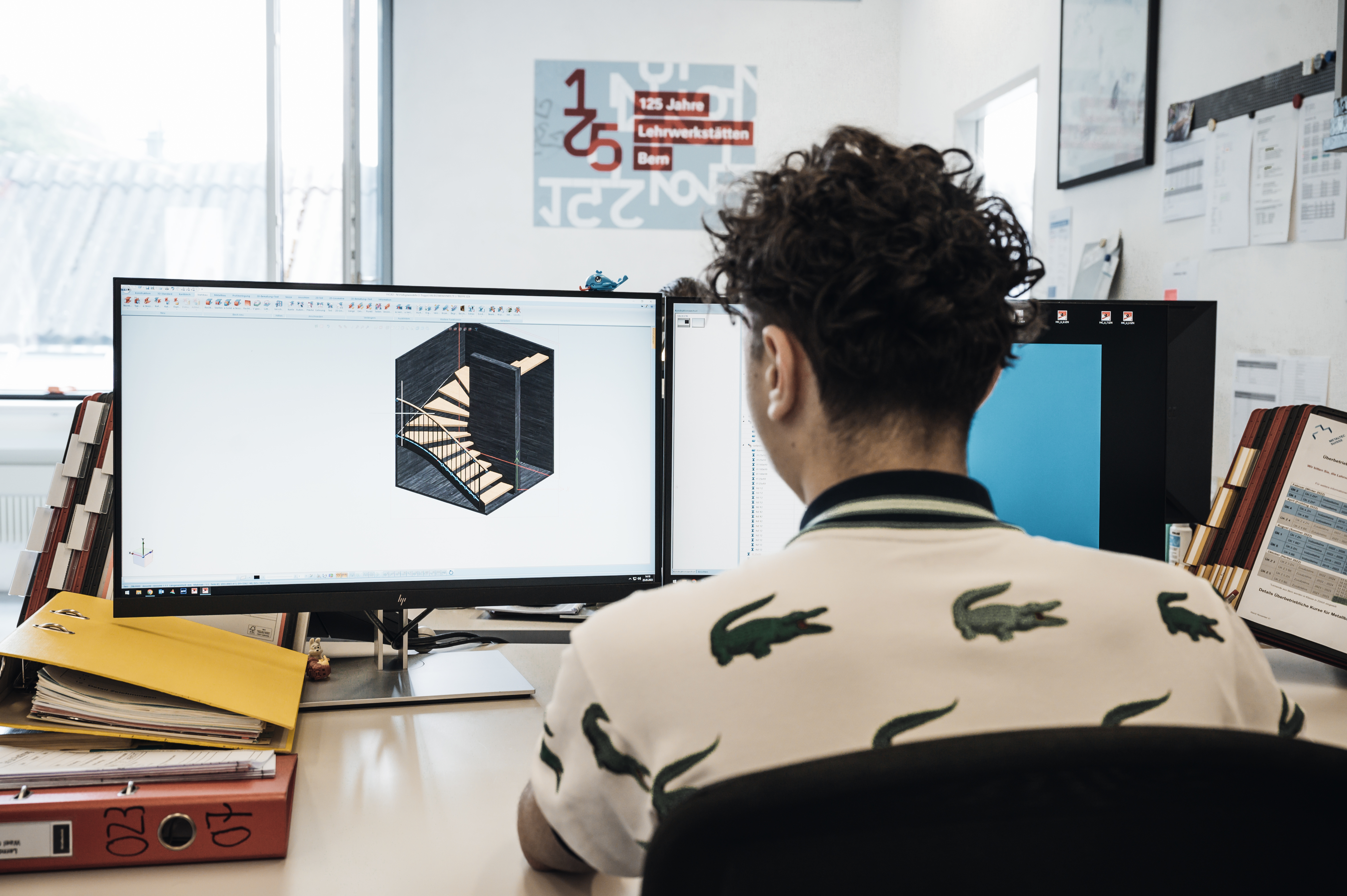 Ein Lernender sitzt vor dem Computer und schaut einen Konstruktionsplan an