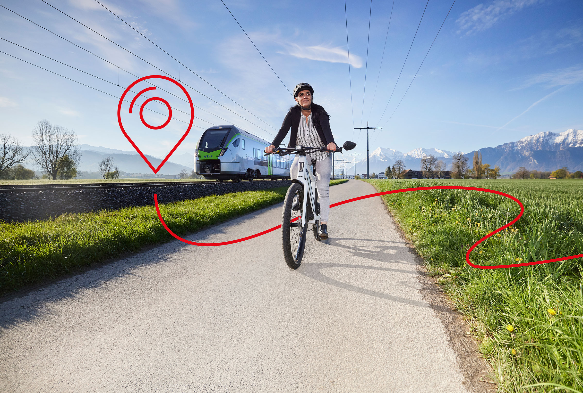 Une femme est à vélo sur un chemin de campagne. Un train est visible à l'arrière-plan.